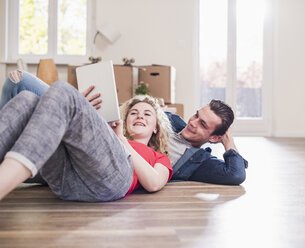 Glückliches junges Paar in neuer Wohnung mit Tablet auf dem Boden liegend - UUF10740