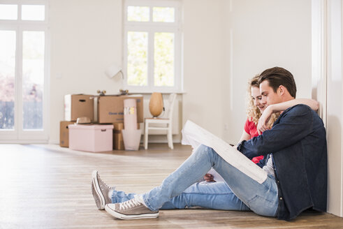 Junges Paar in neuem Haus sitzt auf dem Boden und betrachtet den Grundriss - UUF10743