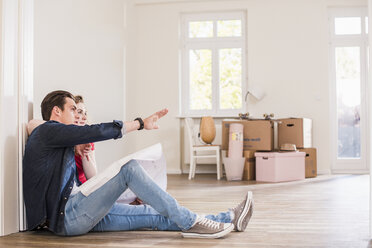 Young couple in new home sitting on floor discussing ground plan - UUF10744