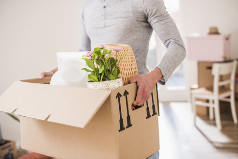 Young man carrying cardboard box in new home - UUF10753
