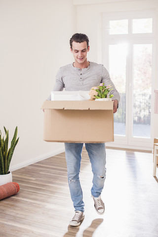 Junger Mann trägt Karton im neuen Zuhause, lizenzfreies Stockfoto