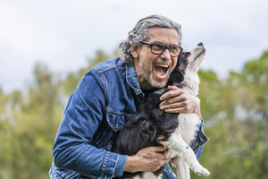Porträt eines glücklichen älteren Mannes, der seinen Hund knuddelt - TCF05414