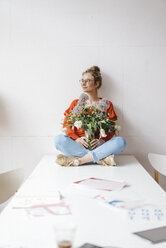 Junge Frau sitzt auf einem Tisch und hält eine Blumenvase - KNSF01512