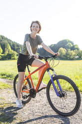 Portrait of smiling young woman with mountain bike - TCF05419