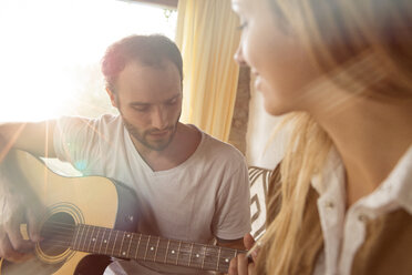 Man playing guitar at home while his girlfriend watching him - ZOCF00413