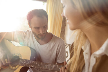 Mann spielt zu Hause Gitarre, während seine Freundin ihn beobachtet - ZOCF00413