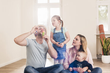 Family blowing soap bubbles in new home - UUF10787