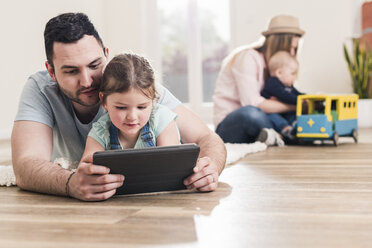 Vater und Tochter benutzen ein Tablet in ihrem neuen Haus mit einer Frau und einem Baby im Hintergrund - UUF10788