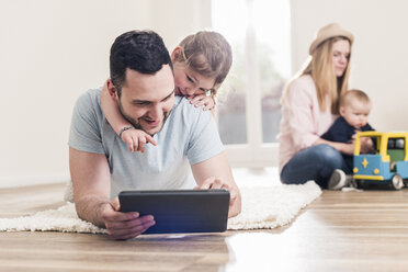 Vater und Tochter benutzen ein Tablet in ihrem neuen Haus mit einer Frau und einem Baby im Hintergrund - UUF10789