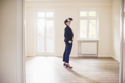 Woman in empty apartment wearing VR glasses - UUF10800