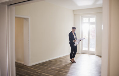 Frau in leerer Wohnung mit Blick auf einen Plan - UUF10805