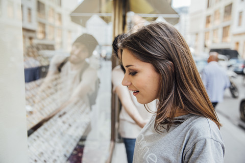 Junge Frau schaut fasziniert in ein Schaufenster, ihr Freund versucht, sie wegzuziehen, lizenzfreies Stockfoto