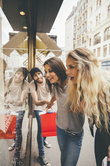 Junge Frauen schauen fasziniert in ein Schaufenster, ihr Freund versucht, sie wegzuziehen - AIF00432