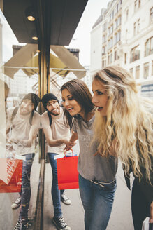 Young women looking fascinated in shop window, boyfriend trying to pull her away - AIF00432