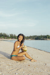 Lächelnde Frau mit Getränk am Strand sitzend - MOMF00170