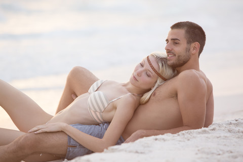 Junges Paar am Strand sitzend, sich umarmend, lizenzfreies Stockfoto