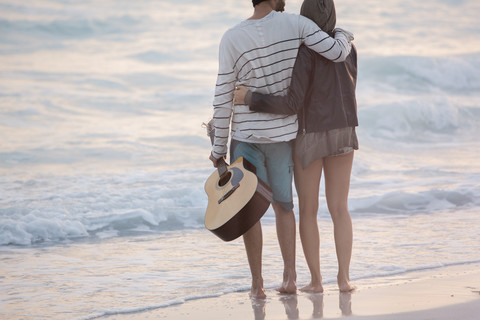 Junges Paar mit Blick auf das Meer mit den Armen um, lizenzfreies Stockfoto