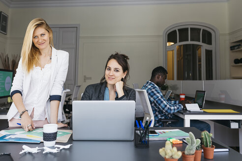 Junge Geschäftsfrauen arbeiten zusammen, benutzen einen Laptop, ein Kollege sitzt im Hintergrund - JRFF01369