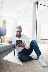 Businessman sitting on floor, using digital tablet - JOSF00998