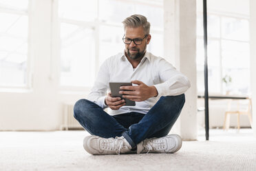 Businessman sitting on floor, using digital tablet - JOSF01005