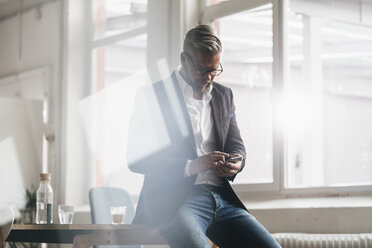 Businessman in office using smartphone - JOSF01009