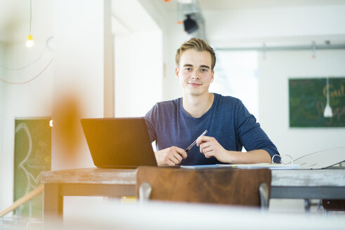 Porträt eines lächelnden Studenten, der mit einem Laptop arbeitet - JOSF01030