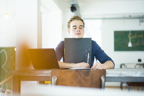 Porträt eines Studenten mit Laptop und Akte in einem Café - JOSF01033