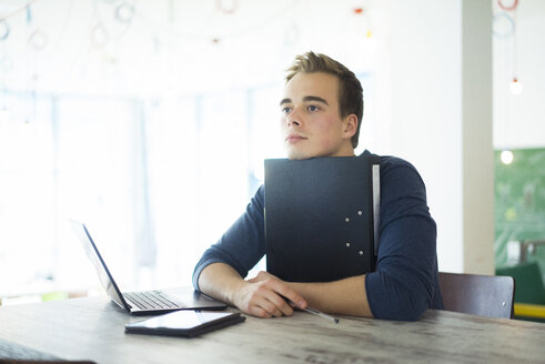 Porträt eines gelangweilten Studenten mit Akte, Laptop und Tablet - JOSF01034