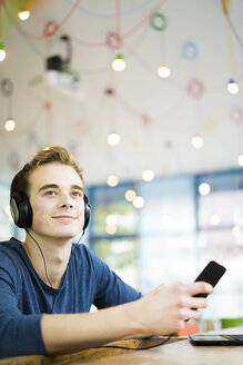 Porträt eines entspannten jungen Mannes, der mit Kopfhörern und Smartphone in einem Café Musik hört - JOSF01042