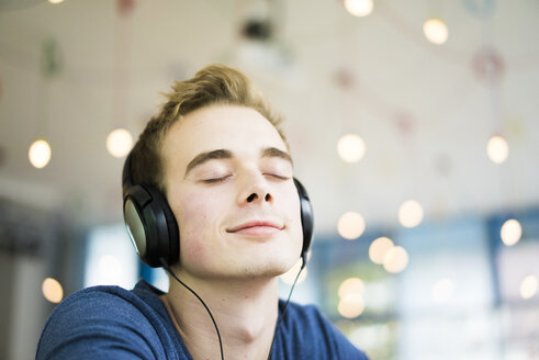 Porträt eines lächelnden jungen Mannes mit geschlossenen Augen, der mit Kopfhörern Musik hört - JOSF01043