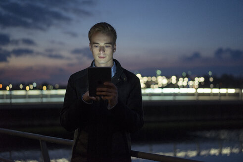 Porträt eines jungen Mannes, der in der Dämmerung im Freien ein Tablet benutzt - JOSF01046