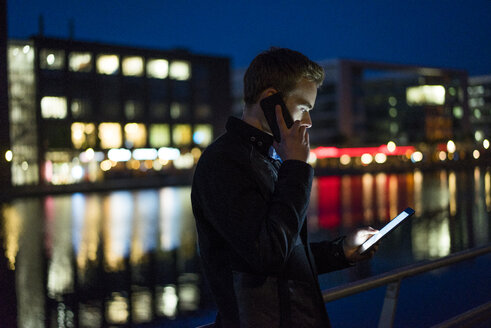 Junger Mann am Telefon mit Blick auf Tablet in der Nacht - JOSF01047