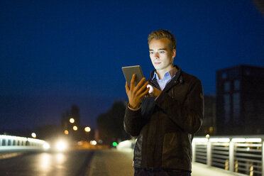 Young man using tablet qutdoors at night - JOSF01048