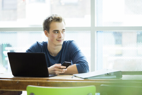 Porträt eines Studenten mit Laptop und Mobiltelefon in einem Café - JOSF01051