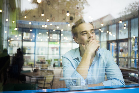 Porträt eines nachdenklichen jungen Mannes, der in einem Café sitzt und durch das Fenster schaut, lizenzfreies Stockfoto