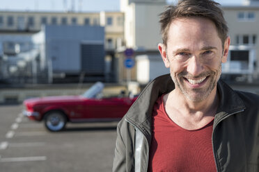 Portrait of smiling mature man in front of his sports car on parking level - FMKF04150