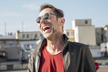 Porträt eines lachenden reifen Mannes mit Bartstoppeln und Sonnenbrille - FMKF04151