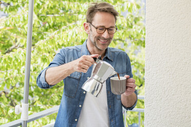 Smiling mature man on balcony pouring coffee in a cup - FMKF04156