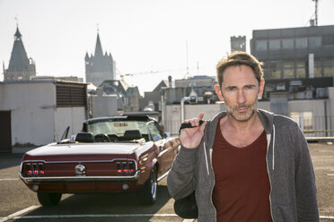 Germany, Cologne, portrait of mature man in front of his parked sports car on parking level - FMKF04157