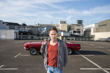 Portrait of mature man in front of his sports car on parking level - FMKF04158