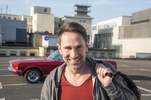 Porträt eines lächelnden reifen Mannes vor seinem Sportwagen auf einem Parkdeck, lizenzfreies Stockfoto