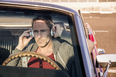 Portrait of mature man sitting in his sports car listening music with head phones - FMKF04162