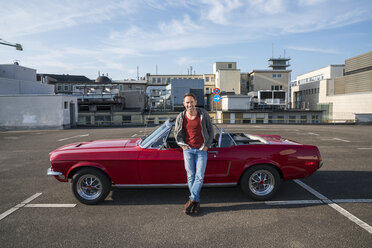 Portrait of smiling mature man leaning against his parked sports car - FMKF04164