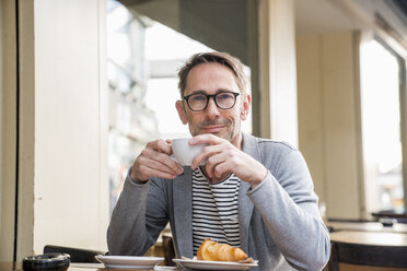 Porträt eines lächelnden reifen Mannes, der in einem Straßencafé Kaffee trinkt - FMKF04168