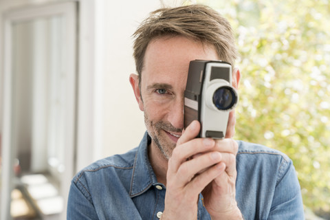 Porträt eines lächelnden Mannes mit Filmkamera, der den Betrachter ansieht, lizenzfreies Stockfoto