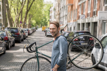 Portrait of smiling mature man carrying his bicycle on the shoulder - FMKF04187