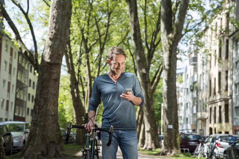 Smiling mature man with bicycle in the city looking at cell phone stock photo