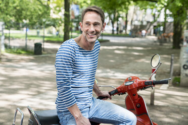 Portrait of smiling mature man with motor scooter - FMKF04192