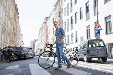 Portrait of smiling mature man with bicycle crossing the street - FMKF04193