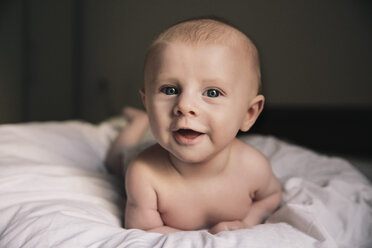 Porträt eines lachenden kleinen Jungen auf dem Bett liegend - MFF03595